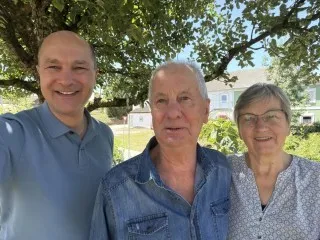 Drei Personen lächeln vor einem Haus im Grünen in Österreich.