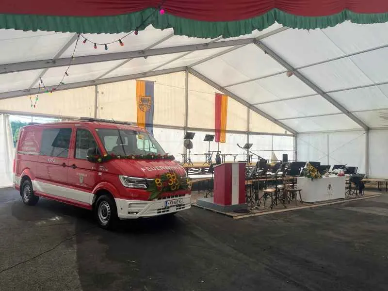Feuerwehr-Einsatzfahrzeug vor Bühne mit Musikerbestuhlung und Rednerpult in Festzelt
