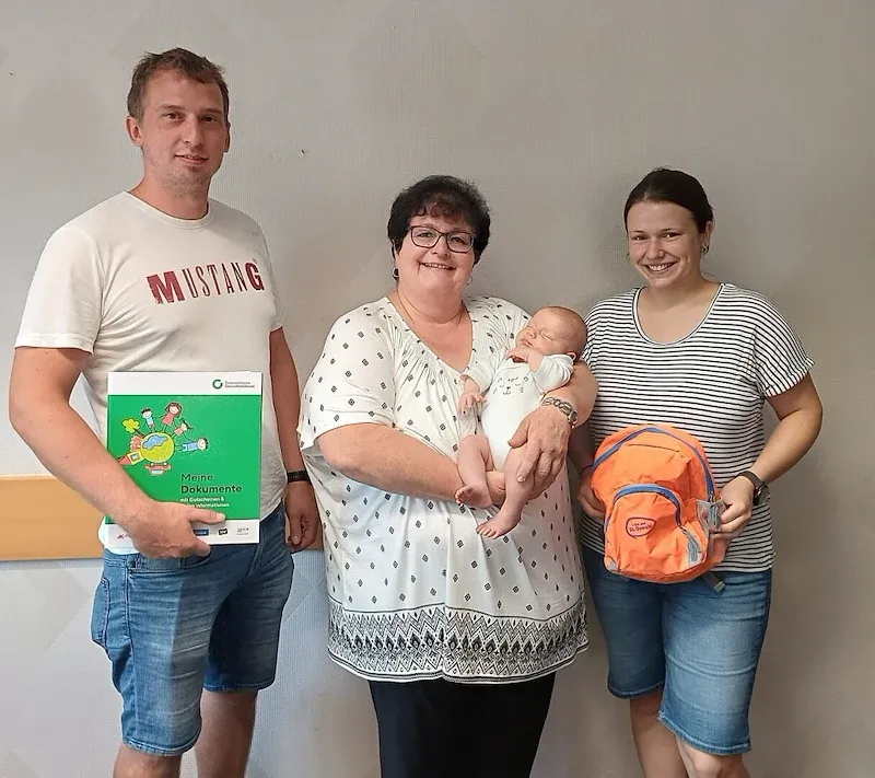 Baby mit Eltern und Betreuerin in Niederösterreich halten Dokumente und Rucksack