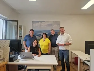 Teamfoto: Fünf Personen stehen in einem Büro in Österreich, im Hintergrund ein Bergpanorama.