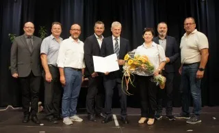 Auszeichnung für verdiente Persönlichkeiten in Niederösterreich: Eine Gruppe von Männern und eine Frau mit Blumenstrauß vor Bühne.