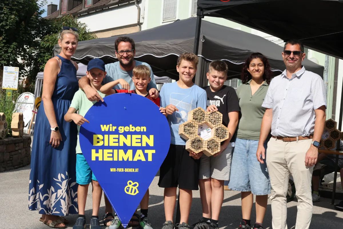 Bienenprojekt: Gruppe mit Kindern und Erwachsenen hält Schild "Wir geben Bienen Heimat" und Insektenhotel