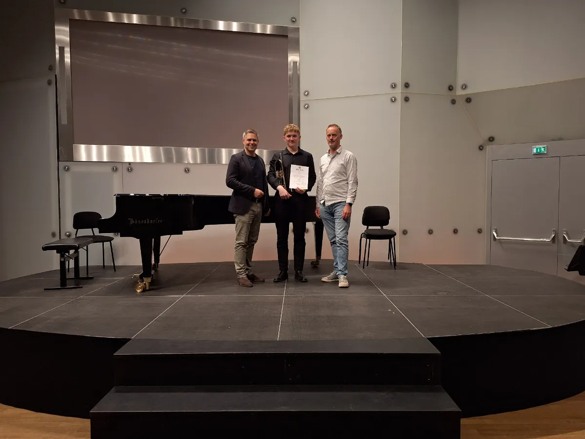 Drei Männer stehen auf einer Bühne vor einem Bösendorfer-Flügel, einer hält eine Urkunde und einen Pokal.