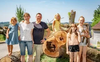 Familie mit vier Kindern und einer Ziege posiert vor einem Baumstamm in der Steiermark.