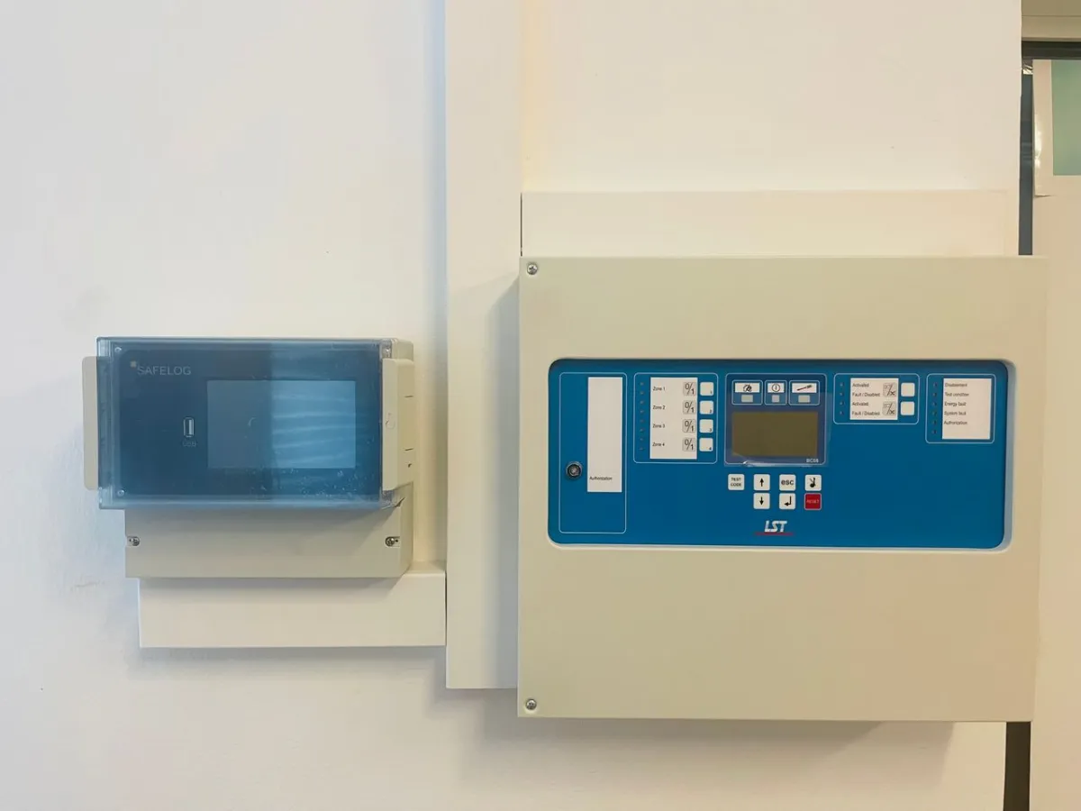 Brandmeldezentrale LST mit SAFELOG-Anzeige an einer weißen Wand montiert.