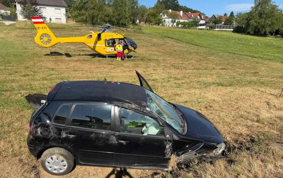 Unfall mit schwarzem Auto und gelbem Rettungshubschrauber auf einer Wiese in Österreich