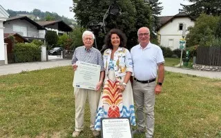 Drei Personen halten Schilder vor einer Skulptur in Oberösterreich.