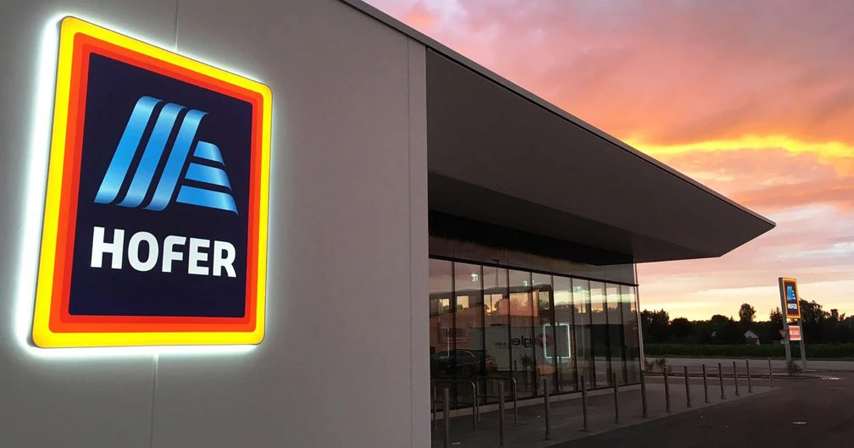 Hofer-Filiale in Österreich mit beleuchtetem Logo vor einem Abendhimmel