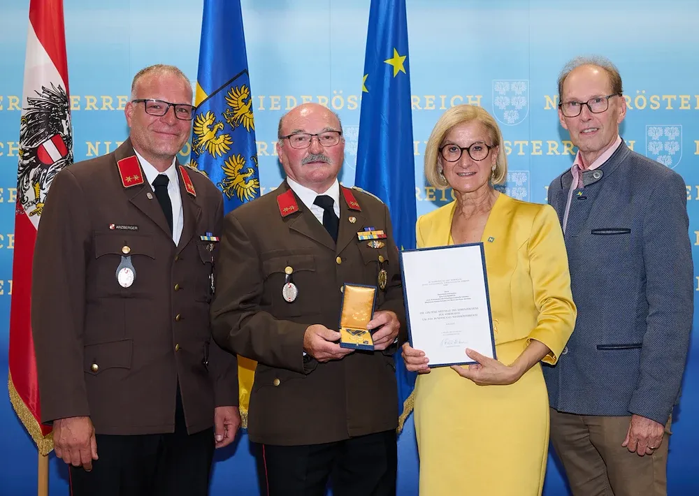 Feuerwehrkommandant Arzberger und weitere Personen mit Urkunde und Ehrenzeichen vor Fahnen in Niederösterreich
