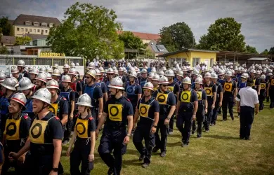 Feuerwehrleute marschieren in Uniform mit Helmen und Schutzkleidung im Freien.