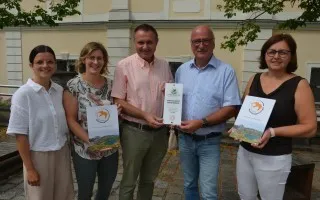 Fünf Personen halten Urkunden vor einem Gebäude in Österreich, zwei Männer und drei Frauen.