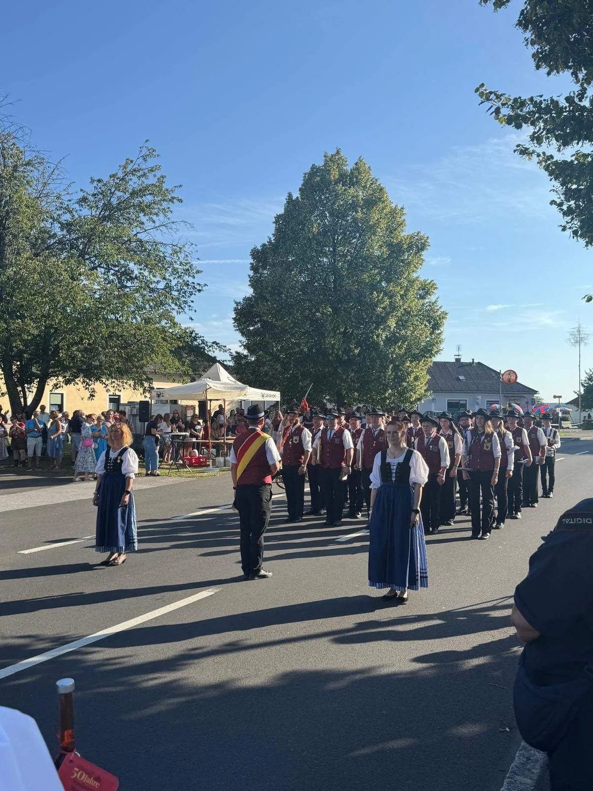Musikkapelle marschiert bei einem Festumzug in Tracht durch eine Ortschaft.