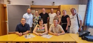Gruppe von neun Personen in einem Raum mit Holzwänden und einer Tafel.