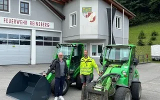 Feuerwehr Reinsberg: Zwei Männer vor zwei grünen Radladern, eines mit Schaufel, vor dem Feuerwehrhaus in Reinsberg.