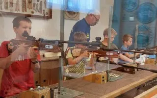 Schützenjugend trainiert im Schützenhaus mit Gewehren, Trainer beaufsichtigt.