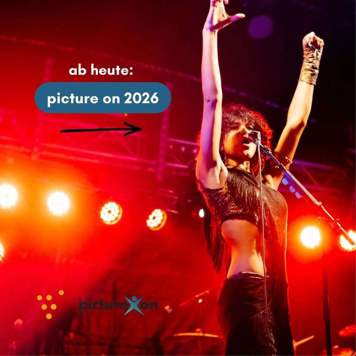 Sängerin mit erhobenen Armen auf Bühne, "picture on 2026"