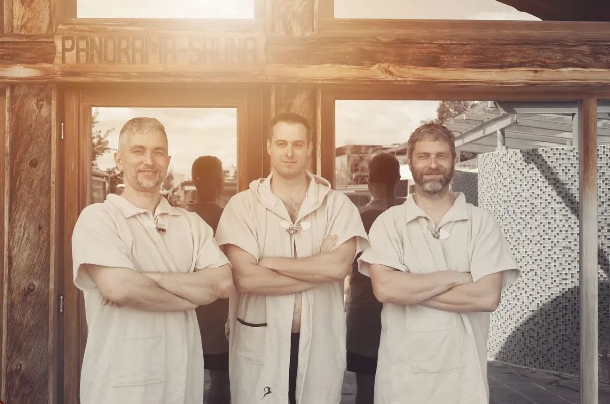 Panorama-Sauna-Team vor Holzhütte in Österreich mit verschränkten Armen