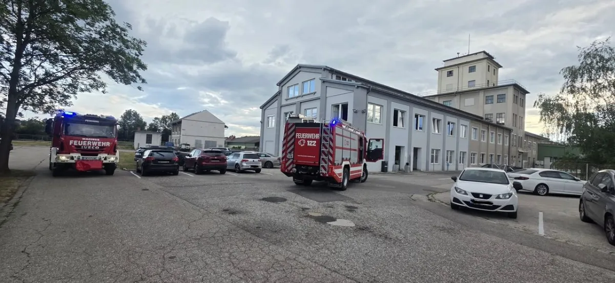 Feuerwehrautos mit Blaulicht parken vor einem Industriegebäude mit mehreren Autos.