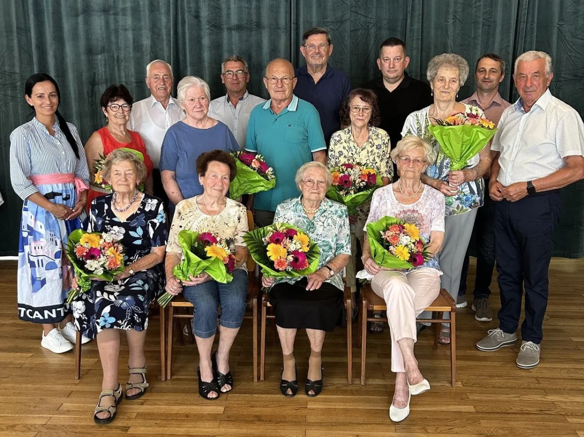 Ehrenamtliche mit Blumensträußen vor grünem Vorhang in Österreich