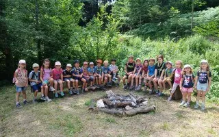 Kindergruppe sitzt bei Lagerfeuerstelle im Wald in Österreich