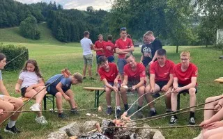 Jugendliche einer Feuerwehr rösten Würstel über einem Lagerfeuer in einem ländlichen Park.