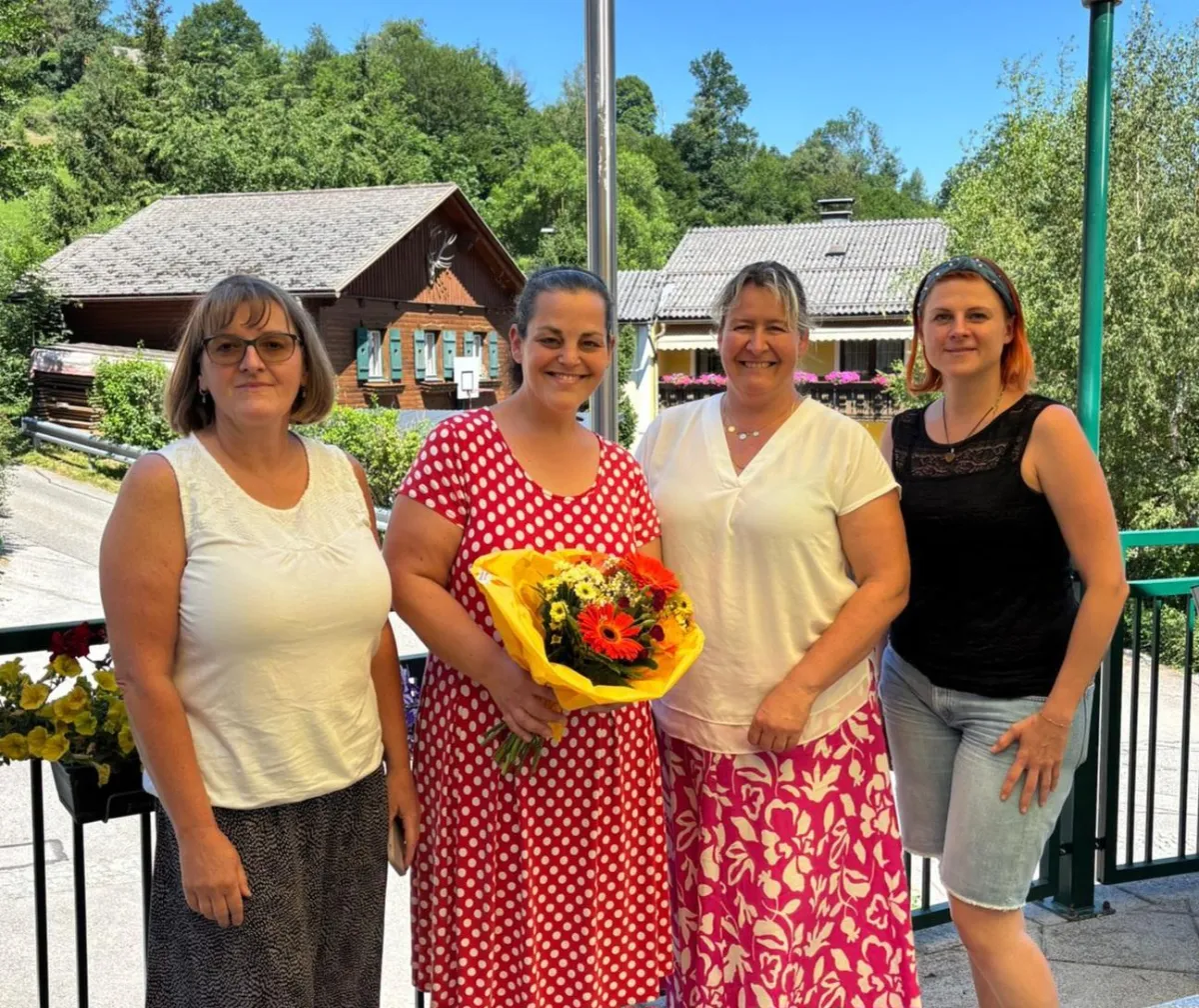 Vier Frauen stehen vor einem Holzhaus in Steiermark, eine hält Blumen.