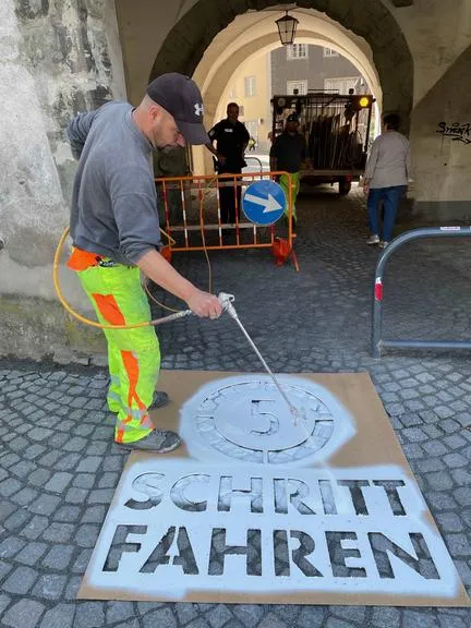 Schritt fahren Markierung mit Sprühfarbe auf Boden, Mann mit Warnweste in Salzburg