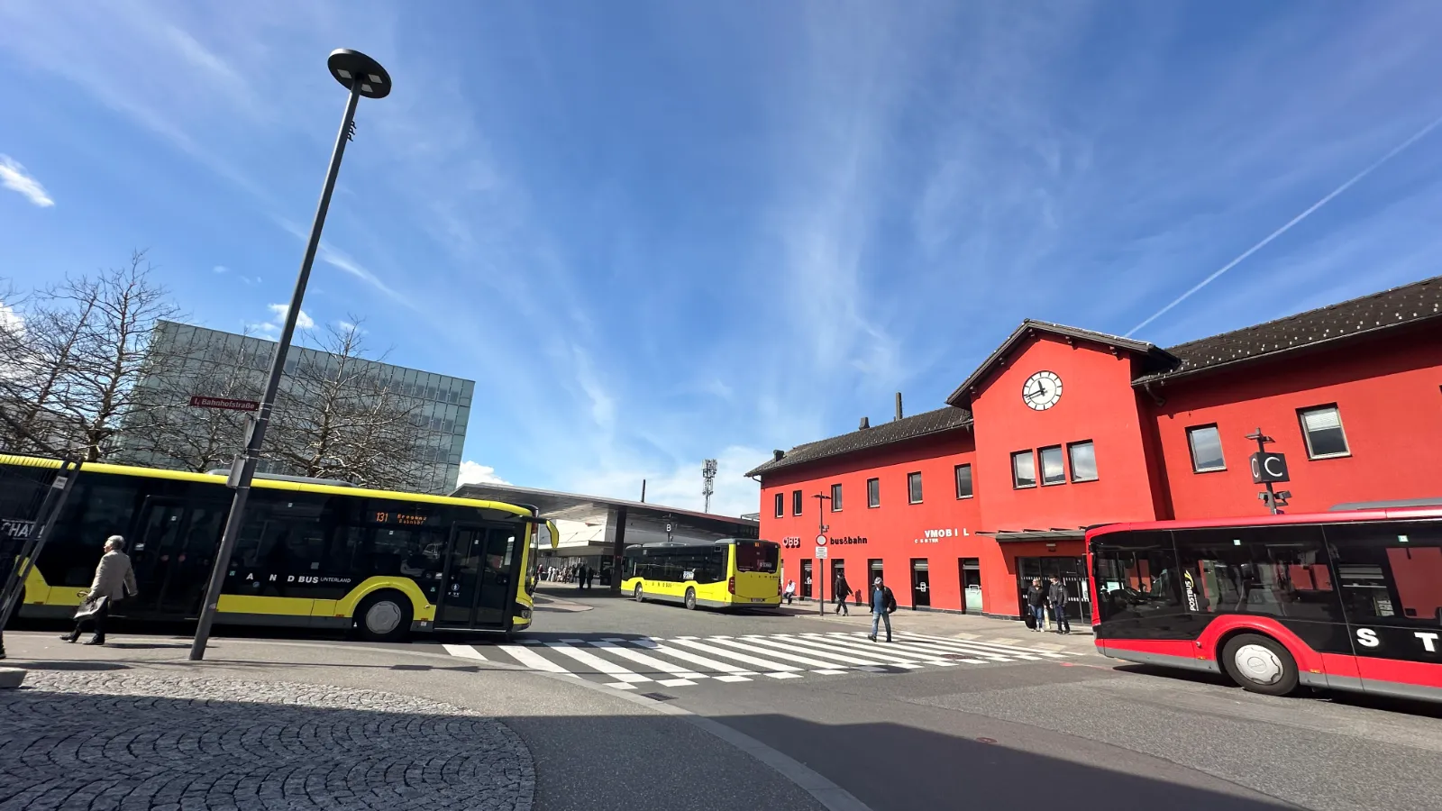 Bahnhof Bregenz mit gelben und roten Bussen vor dem roten Bahnhofsgebäude