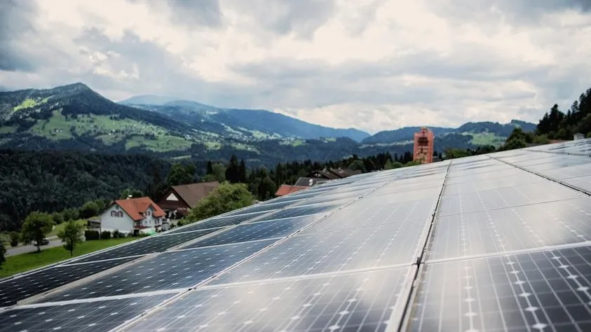 Solaranlage auf einem Dach in den österreichischen Alpen mit Häusern und Bergen im Hintergrund.