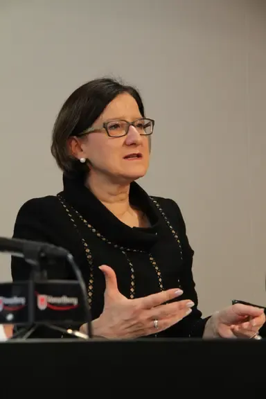 Bundesministerin Karoline Edtstadler mit Brille und schwarzem Kleid gestikuliert bei einer Pressekonferenz im Bundeskanzleramt in Wien.