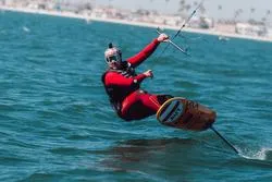 Kitesurfer in rotem Neoprenanzug auf dem Meer bei sonnigem Wetter