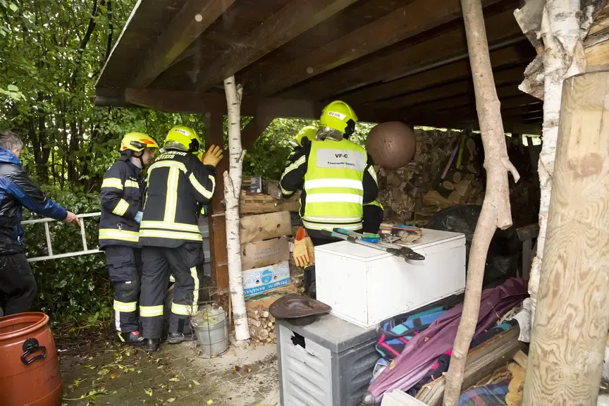 Feuerwehrleute in Schutzkleidung sortieren unter einem Vordach Holz und Gerätschaften.