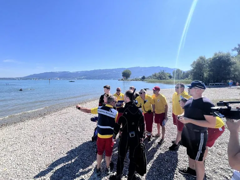 Rettungsschwimmer am Bodensee geben Anweisungen an ein Taucherteam und Kameramann