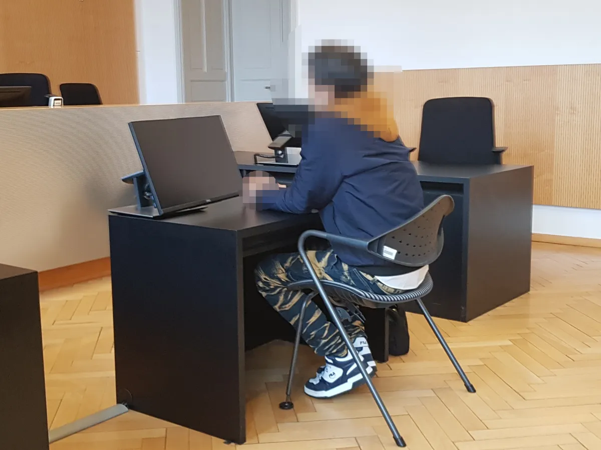 Gerichtsverhandlung: Angeklagter sitzt vor Computerbildschirm in einem Gerichtssaal