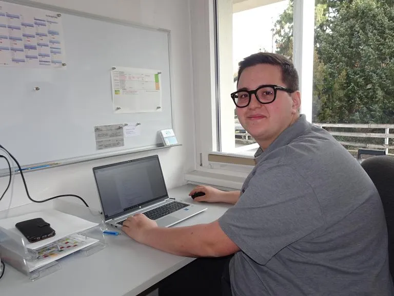 Mann mit Brille am Laptop in Büro mit Kalender an Wand
