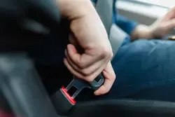 Anschnallen im Auto: Person schließt Sicherheitsgurt in einem Fahrzeug, Detailaufnahme der Hand am Gurtverschluss.
