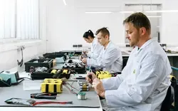 Mitarbeiter mit Laborkitteln arbeiten an Elektronikkomponenten in einem hellen Schulungsraum in Österreich.