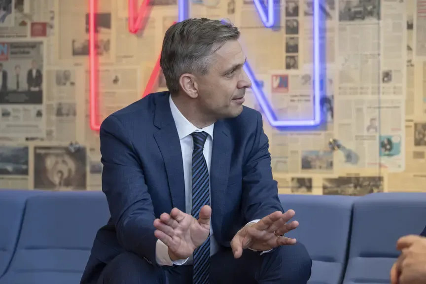 Politiker im Anzug gestikuliert im Gespräch vor Zeitungs-Wand und Neon-Schriftzug in Wien
