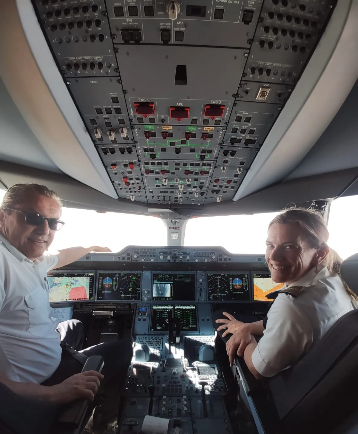 Piloten im Cockpit eines Flugzeugs mit vielen Bildschirmen und Bedienelementen.