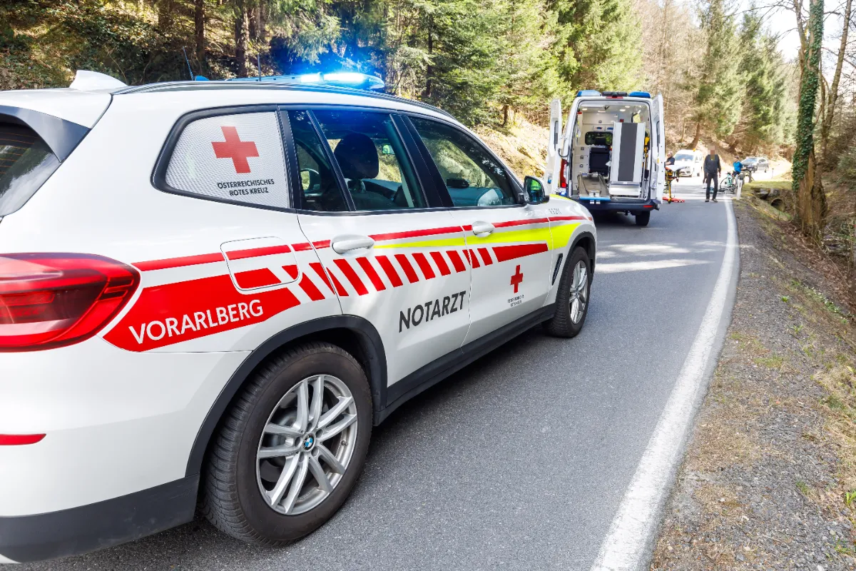 Notarzt-Einsatzfahrzeug des Roten Kreuzes Vorarlberg mit Blaulicht auf einer Straße im Wald