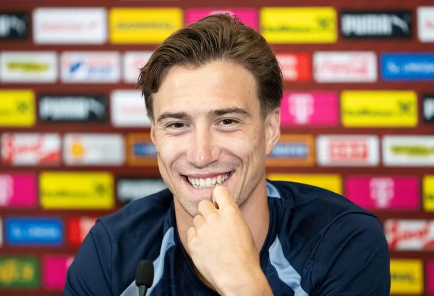 Konrad Laimer lächelnd vor einer Sponsorenwand mit Logos von Puma, Coca-Cola und Magenta