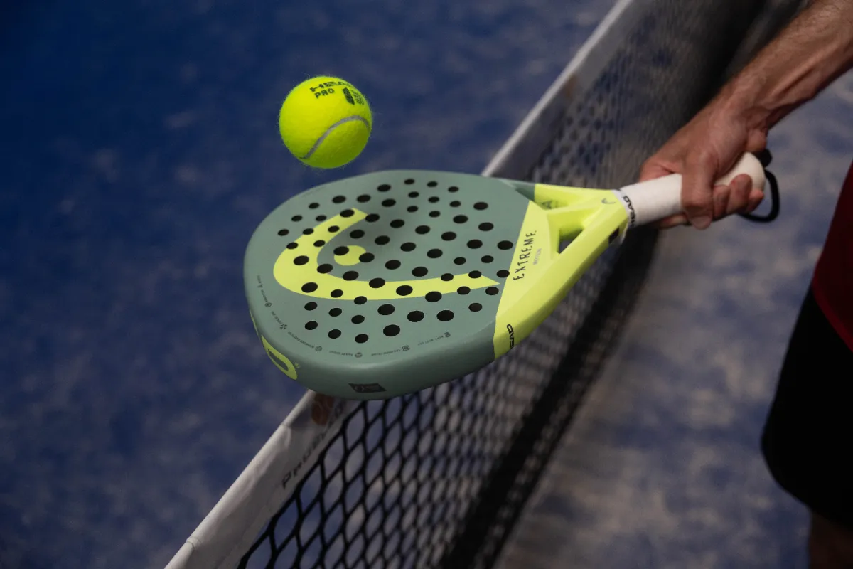 Padel-Schläger und Ball am Netz auf einem blauen Padel-Court