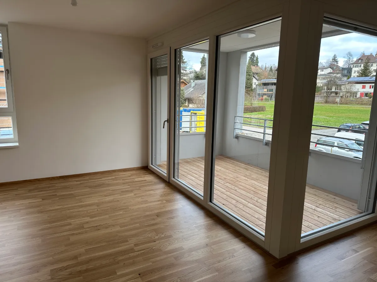 Balkon mit Holzdielen und Blick auf grüne Wiese und Häuser