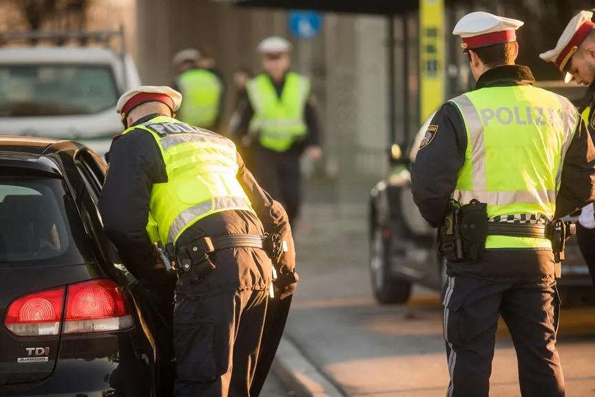 Polizisten in gelben Warnwesten kontrollieren Verkehr auf einer Straße in Österreich.