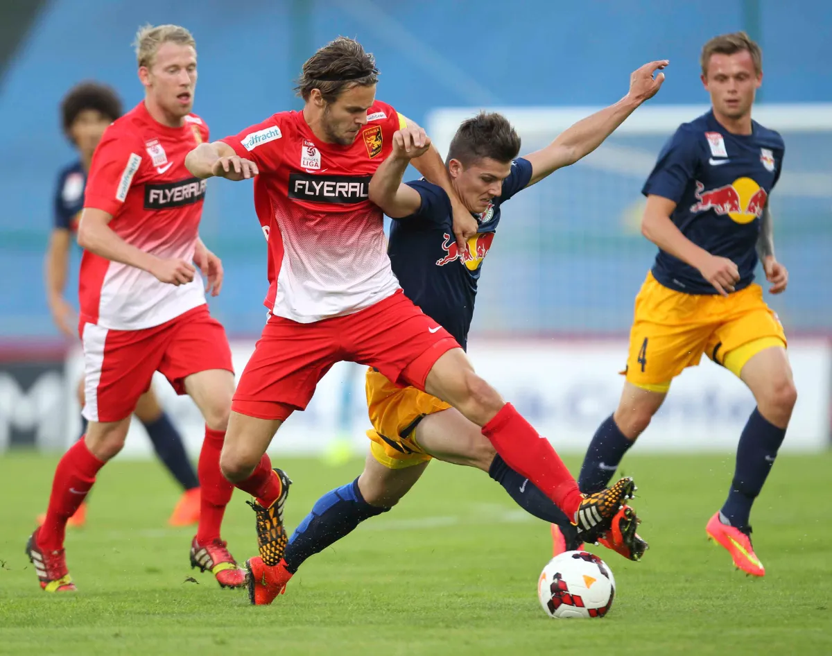 Fußballspieler im roten Dress kämpfen im Spiel um den Ball vor einem Spieler im blauen Dress mit gelber Hose.