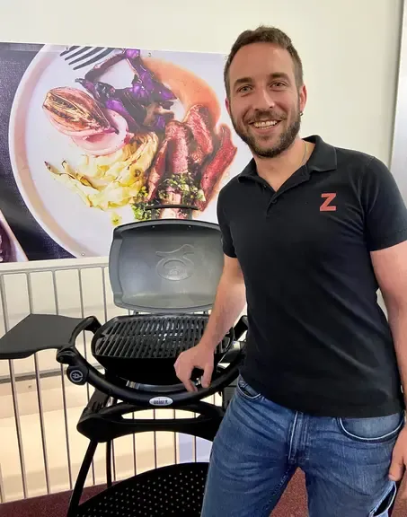 Mann mit Grill vor Speisebild