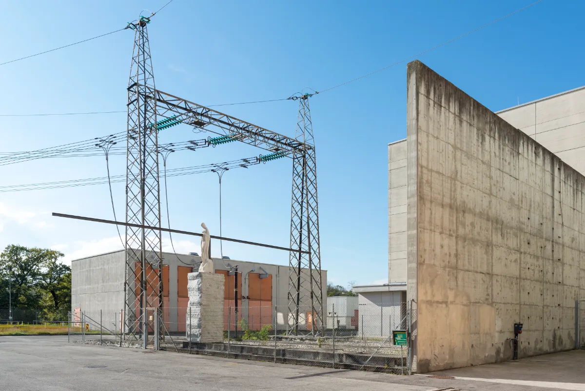 Umspannwerk mit Madonna-Statue und Strommasten vor Betongebäuden