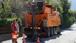 Kanalreinigung in St. Pölten: Zwei Arbeiter beobachten einen orangefarbenen Saug- und Spülwagen auf der Straße.