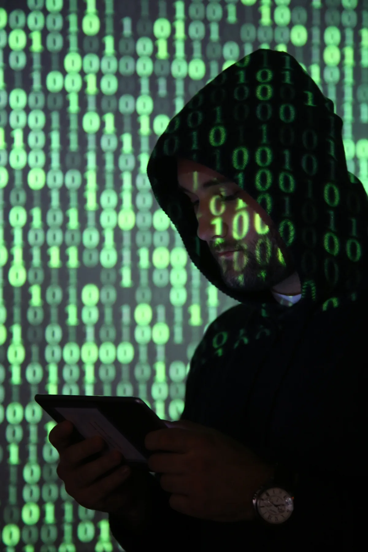 Hacker mit Kapuze und Tablet vor binärem Code-Hintergrund
