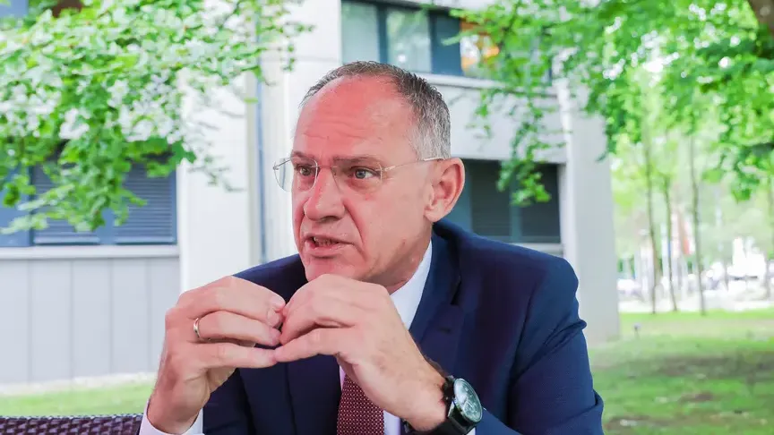 Gerhard Karner spricht im Freien vor einem Gebäude mit Bäumen im Hintergrund.